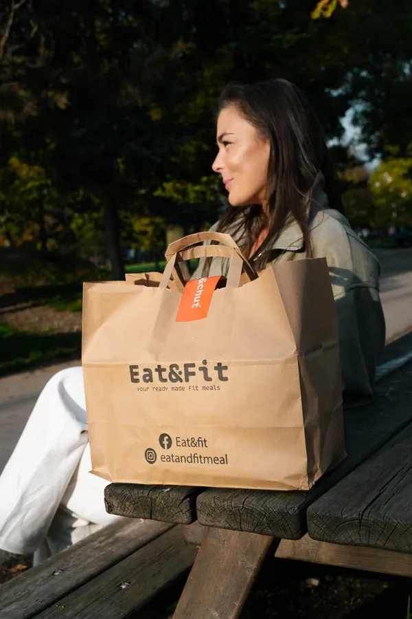 Zákazníčka Eat&Fit sediaca na lavičke v parku s papierovou taškou plnou krabičiek